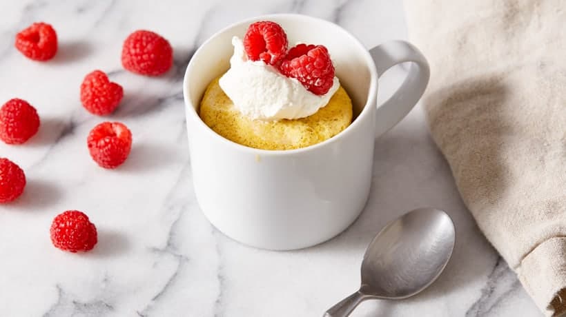 vanilla mug cake topped with whipped cream and berries