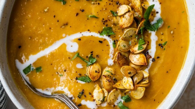 Bowl of acorn squash soup garnished with roasted acorn seeds and parsley.