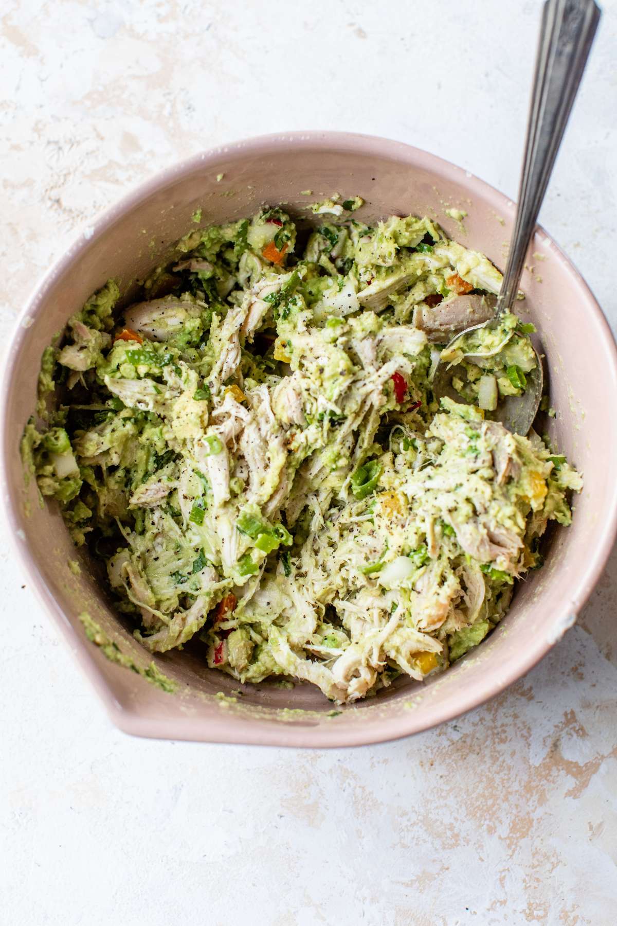 Stirring together mashed avocado with chicken and other salad ingredients.