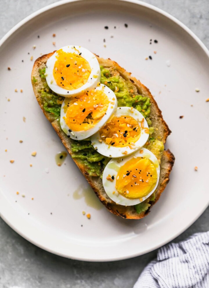 Avocado toast with hard boiled egg on a white plate.