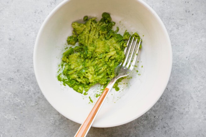 Using a fork to mash avocado in a white bowl.