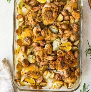 Chicken and potatoes in a glass baking dish near fresh rosemary.