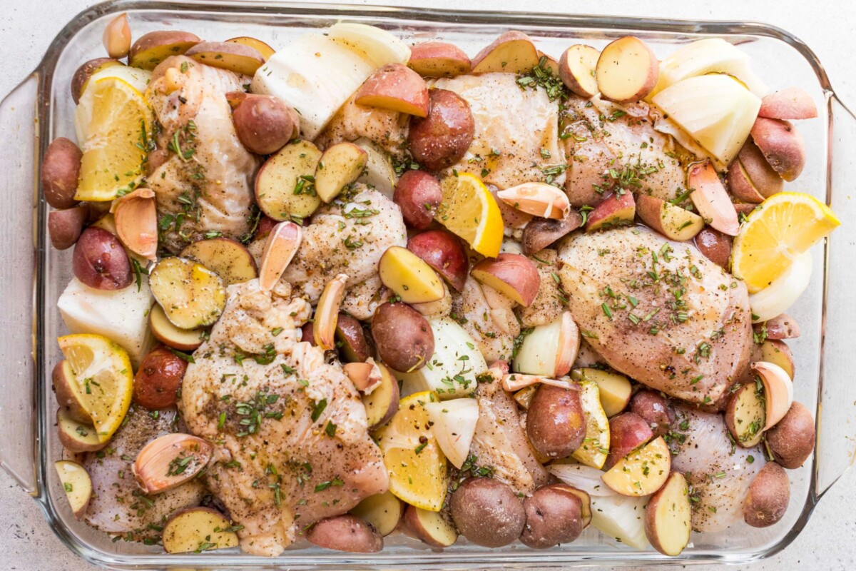 Chicken and veggies seasoned in a glass baking dish.