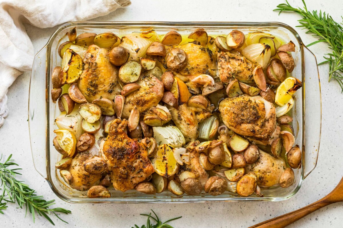 Baked chicken and potatoes with onion in a glass baking dish.
