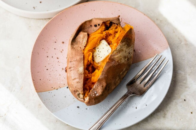 Baked sweet potato with butter on a plate with a fork.
