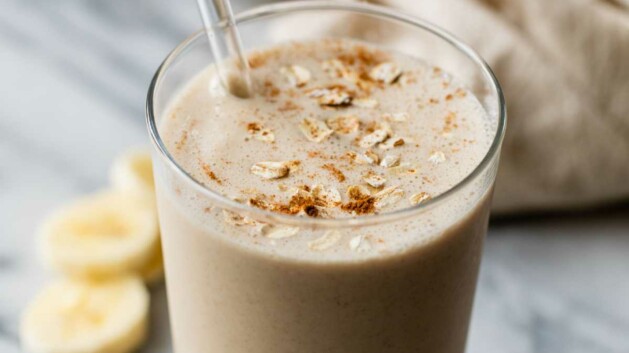 Breakfast smoothie in a glass with a straw garnished with oats and cinnamon.