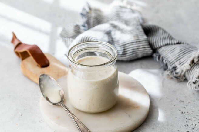 Caesar dressing sitting on a marble cutting board near a spoon.