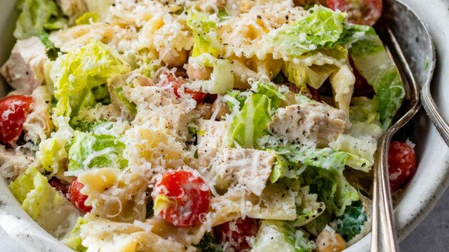 Chicken caesar pasta salad served in a small white bowl with a fork and spoon.