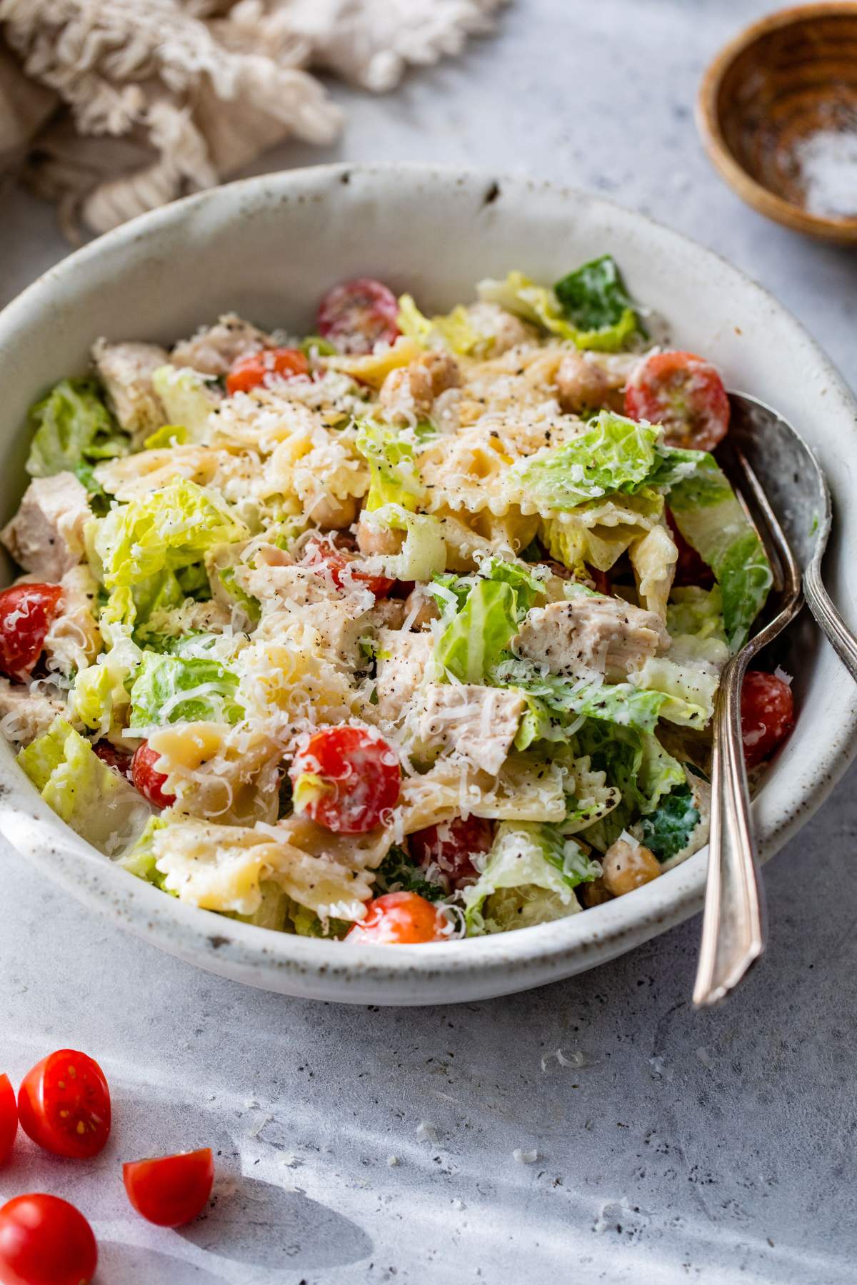 Chicken caesar pasta salad served in a small white bowl with a fork and spoon.