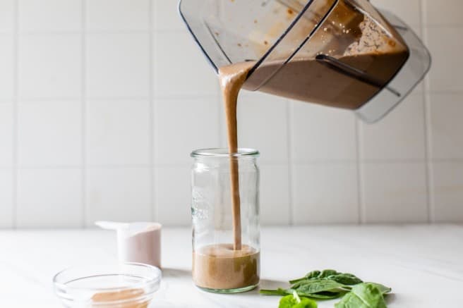 pouring a chocolate protein shake into a glass