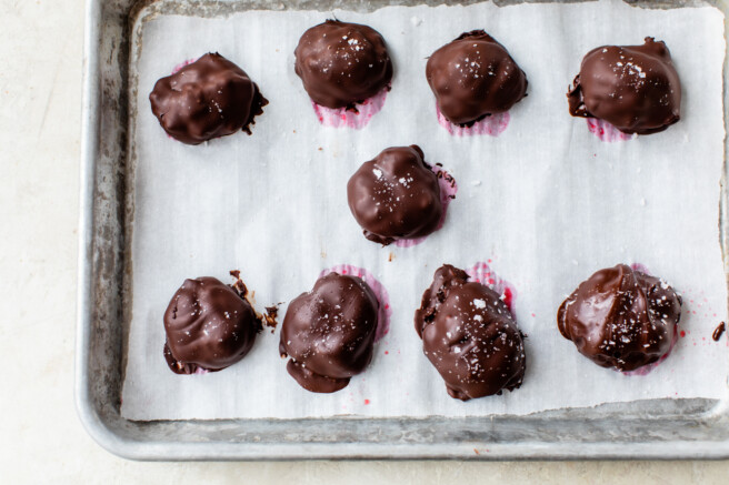 chocolate covered raspberry bites topped with sea salt on a rimmed baking sheet