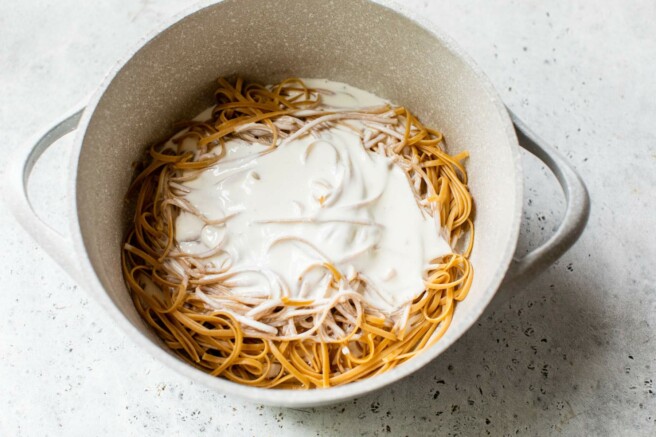 Adding Alfredo with cottage cheese to warm pasta noodles.
