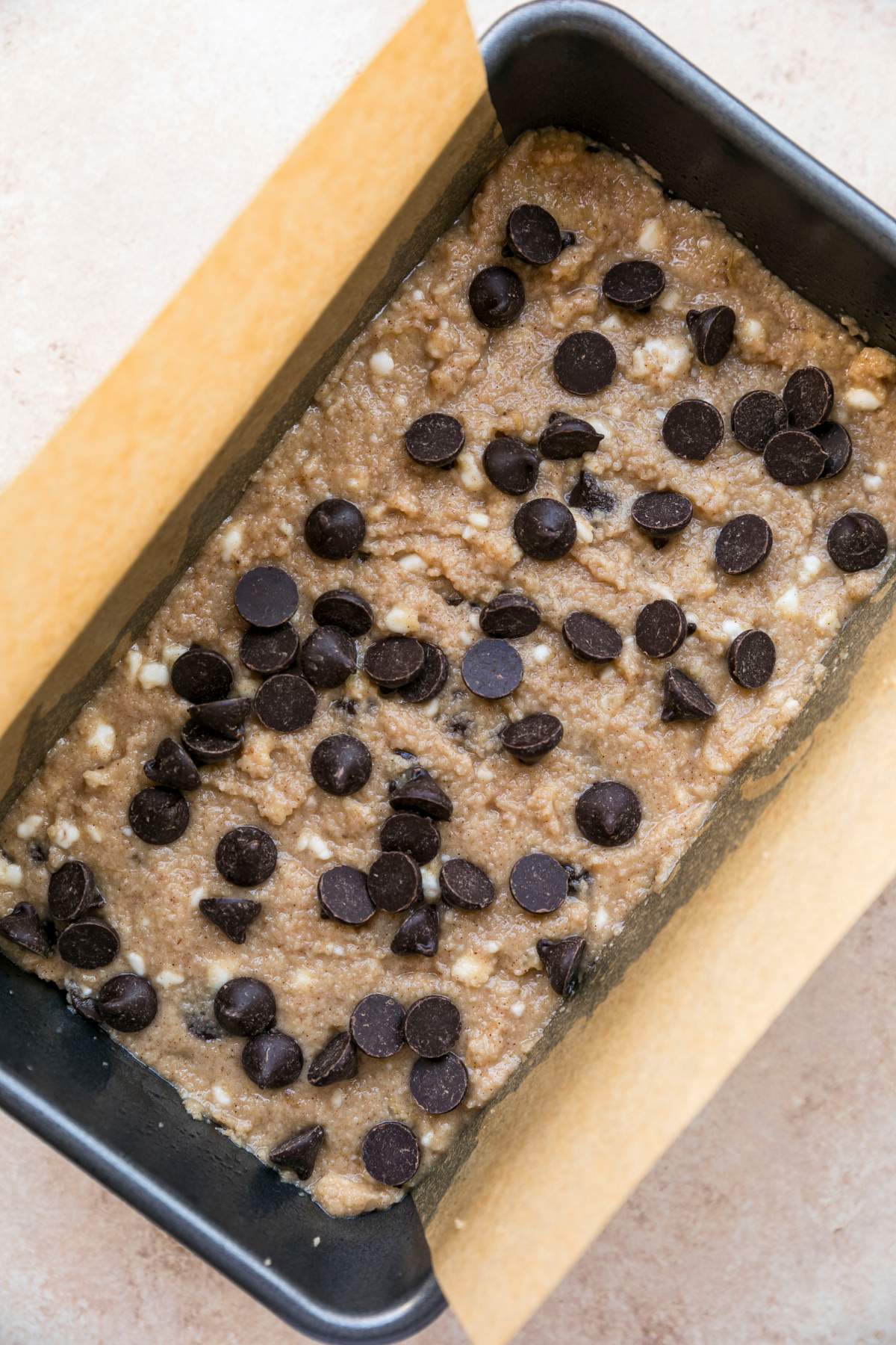 Banana bread batter in a loaf pan lined with parchment.