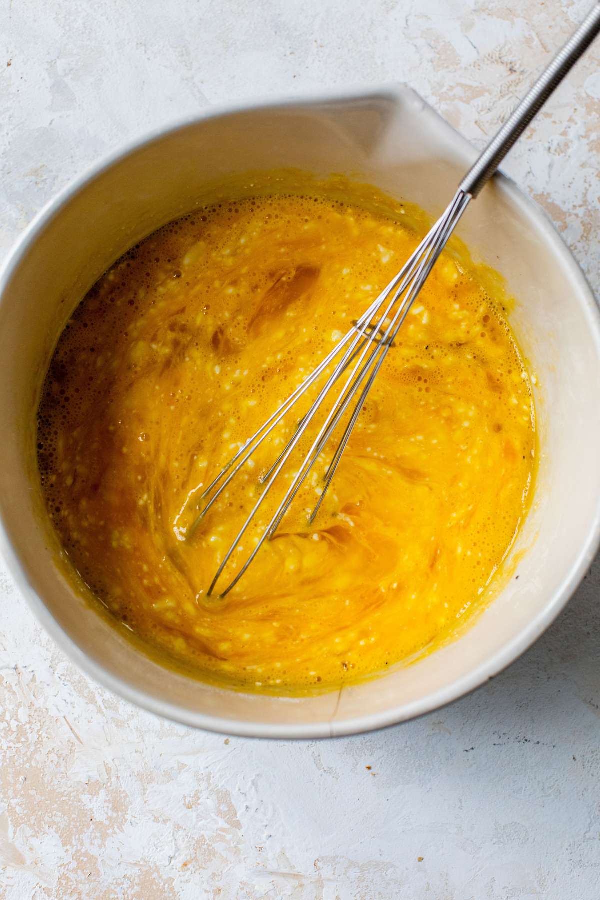 Whisking eggs with cottage cheese in a large bowl.
