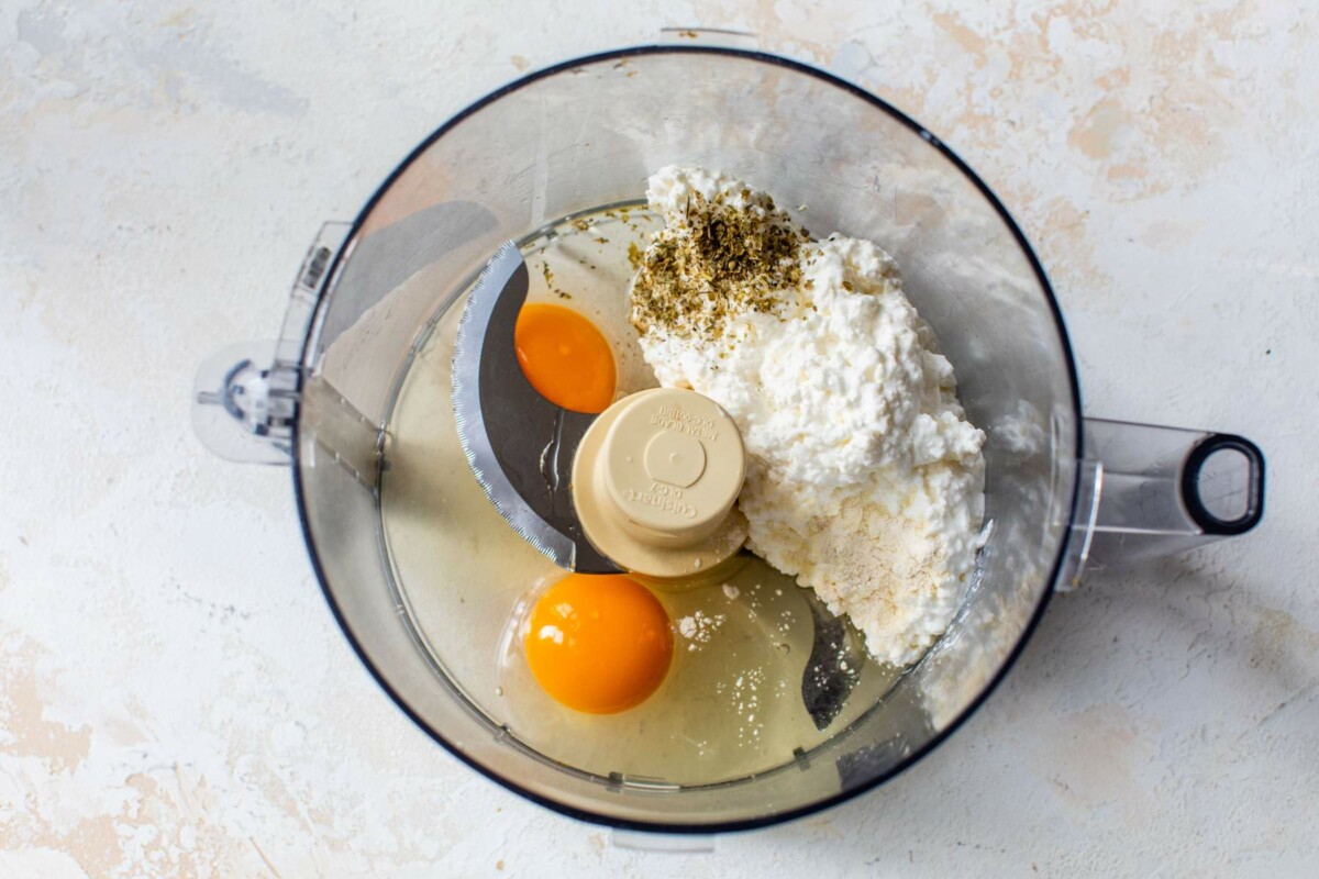Adding eggs, cottage cheese and seasonings to a food processor.