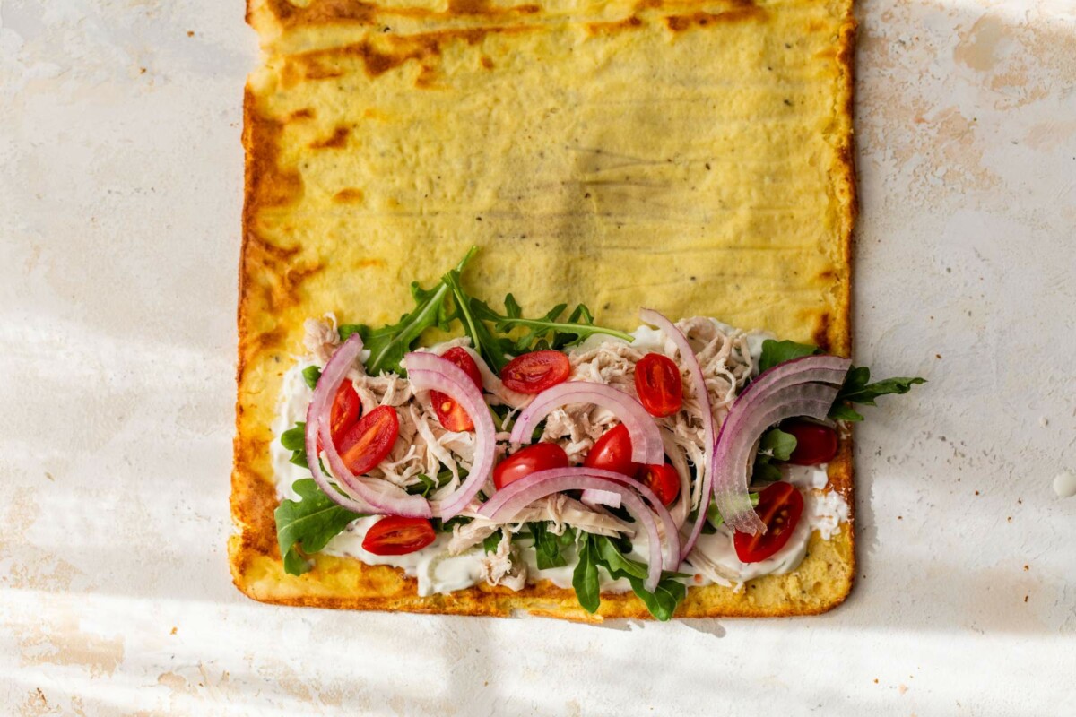 Shredded chicken, tomatoes, arugula and red onions on a wrap.