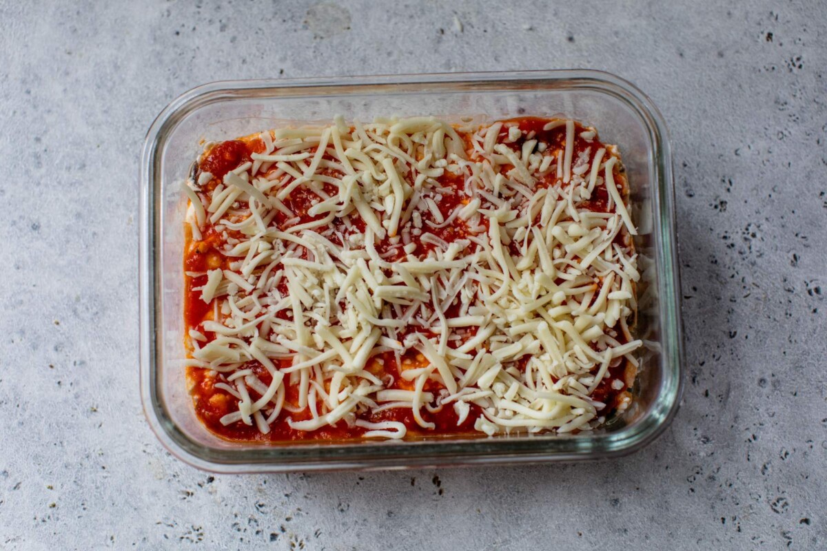 Assembling cottage cheese pizza bowl with marinara and shredded cheese.