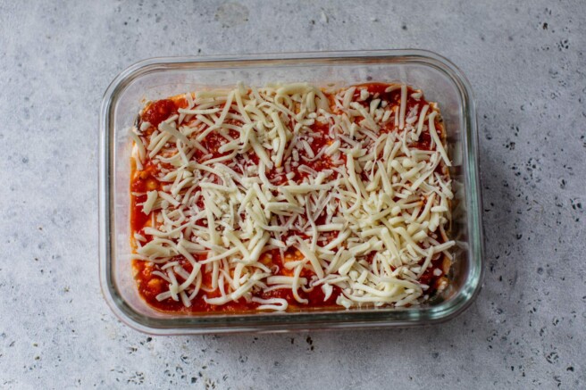 Assembling cottage cheese pizza bowl with marinara and shredded cheese.