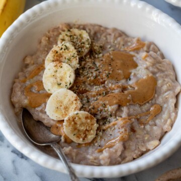 Egg white oatmeal in a white bowl topped with banana slices and almond butter.