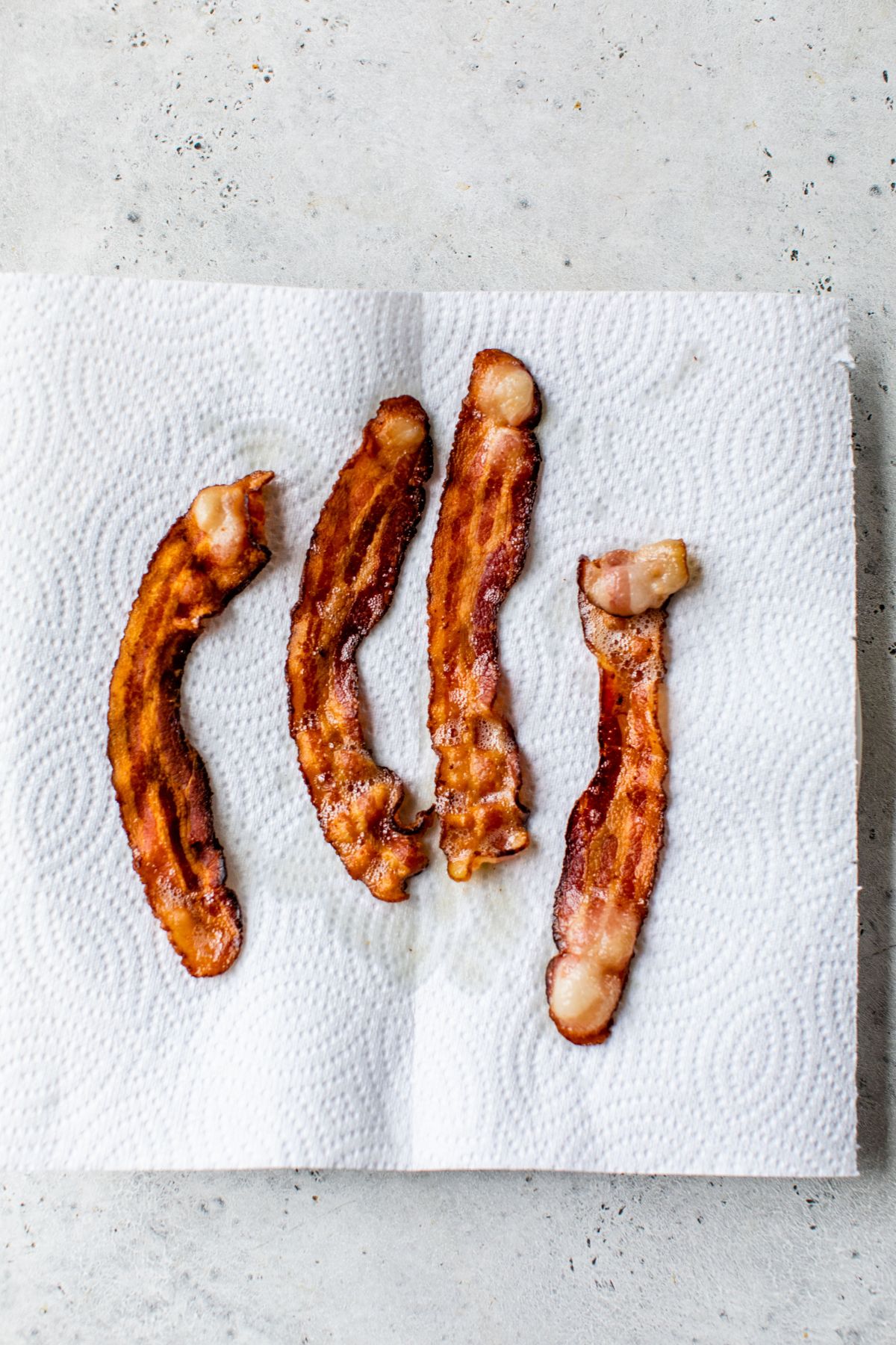 Four slices of cooked bacon on a paper towel.