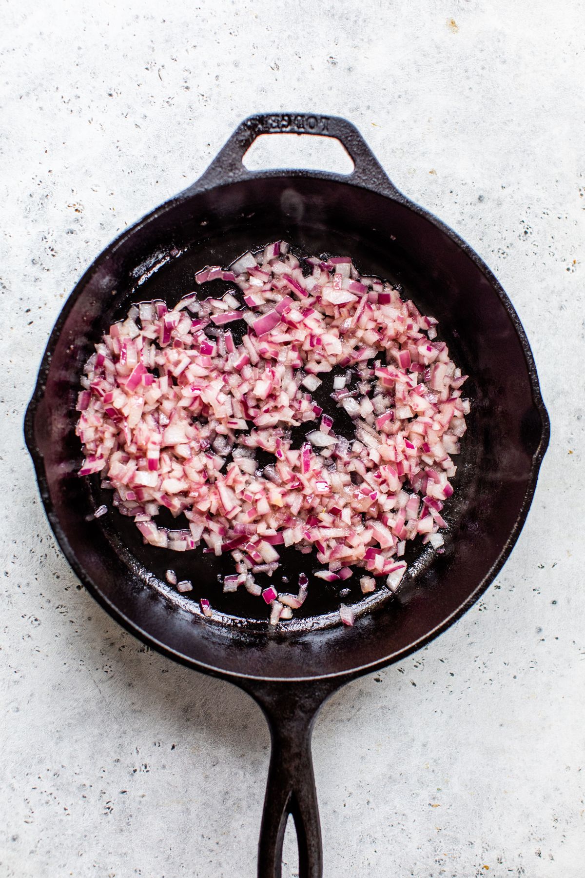 Sautéing diced red onion in a large cast iron skillet.