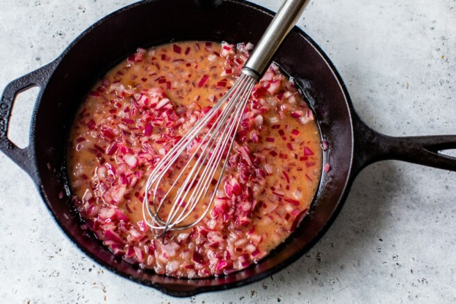 Stirring apple cider vinegar, maple syrup, dijon mustard, salt and pepper with red onion.