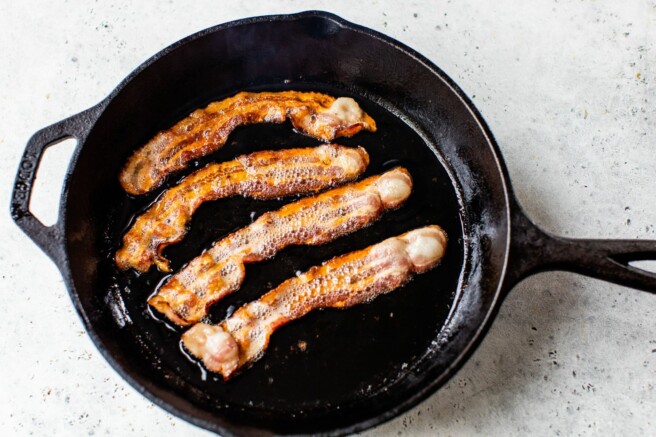Cooking slices of bacon in a large skillet.