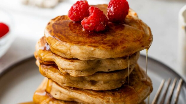 Stack of Greek yogurt pancakes topped with maple syrup and raspberries.