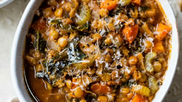 Green lentil soup made with veggies in a white bowl with a spoon.