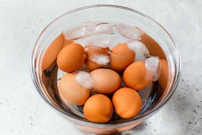 Brown eggs submerged in a large bowl filled with ice water.