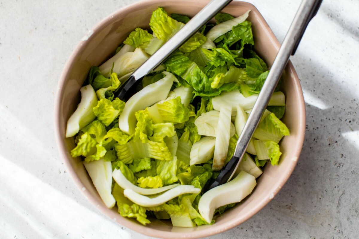 Tongs tossing romaine lettuce with fennel.