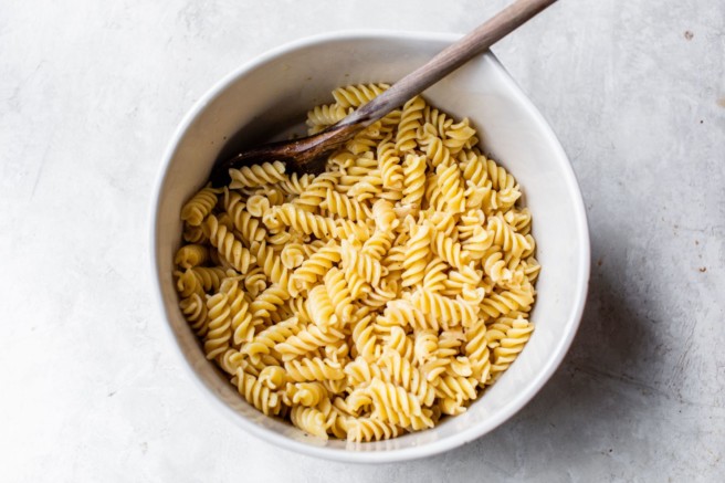 Stirring pasta with dressing in a large bowl.