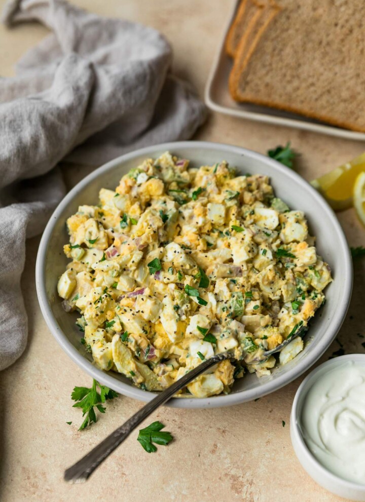 Lightened up egg salad in a bowl near slices of bread.