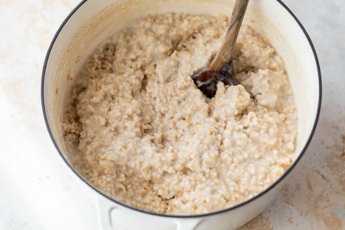 Stirring steel cut oats in a large white pot.