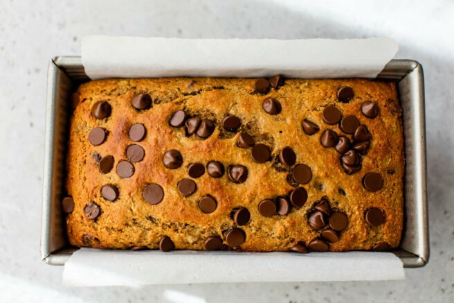 Baked banana bread in a loaf pan lined with parchment paper.