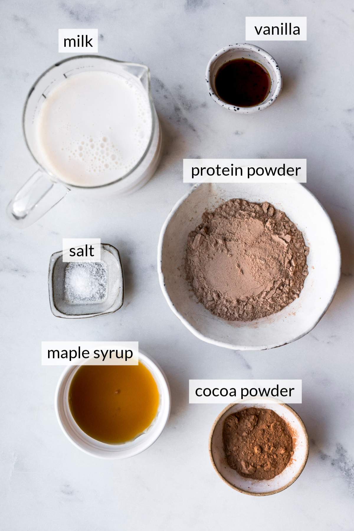 Small bowls with cocoa powder, protein powder, vanilla and milk.