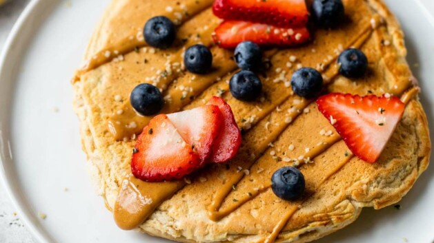 Protein pancake on a white plate with a drizzle of peanut butter and fresh berries.