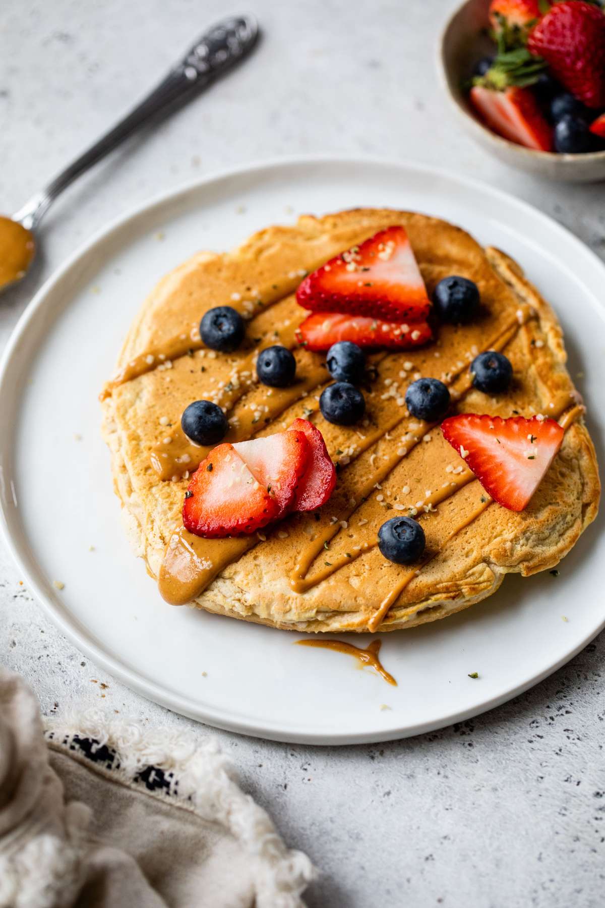 Protein pancake on a white plate with a drizzle of peanut butter and fresh berries.