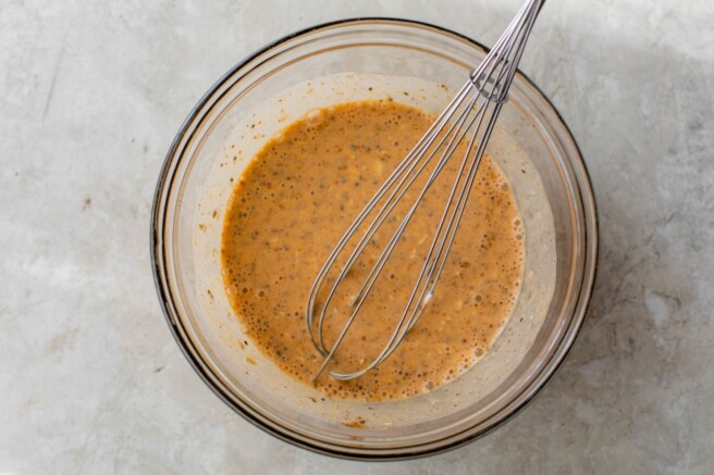 Using a whisk to mix pumpkin puree with oats, greek yogurt and milk.
