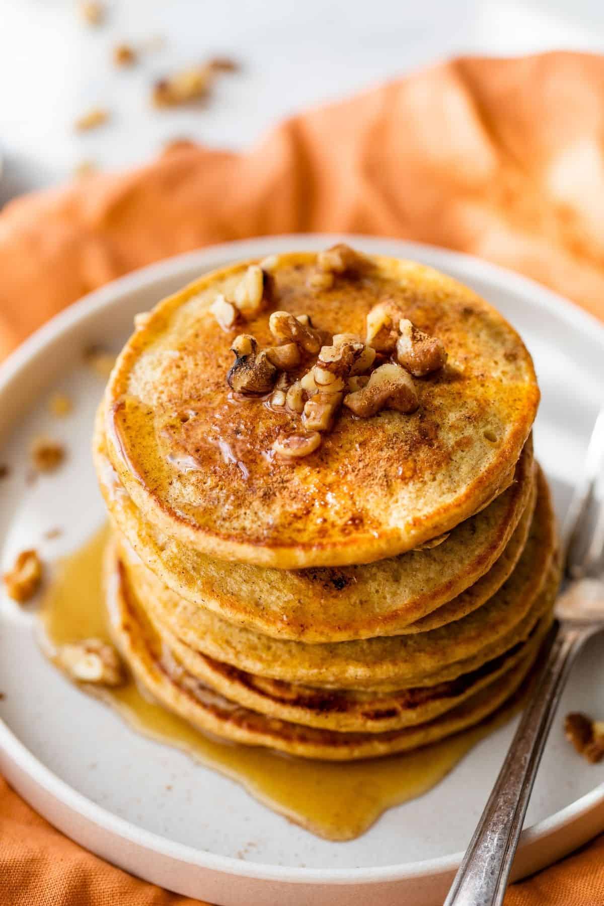 a stack of pumpkin protein pancakes served with chopped walnuts and maple syrup
