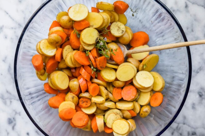 Stirring slices of carrots and baby potatoes in a large bowl.