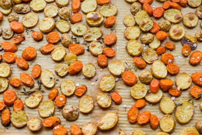 Slices of roasted carrots and baby potatoes on a sheet pan.