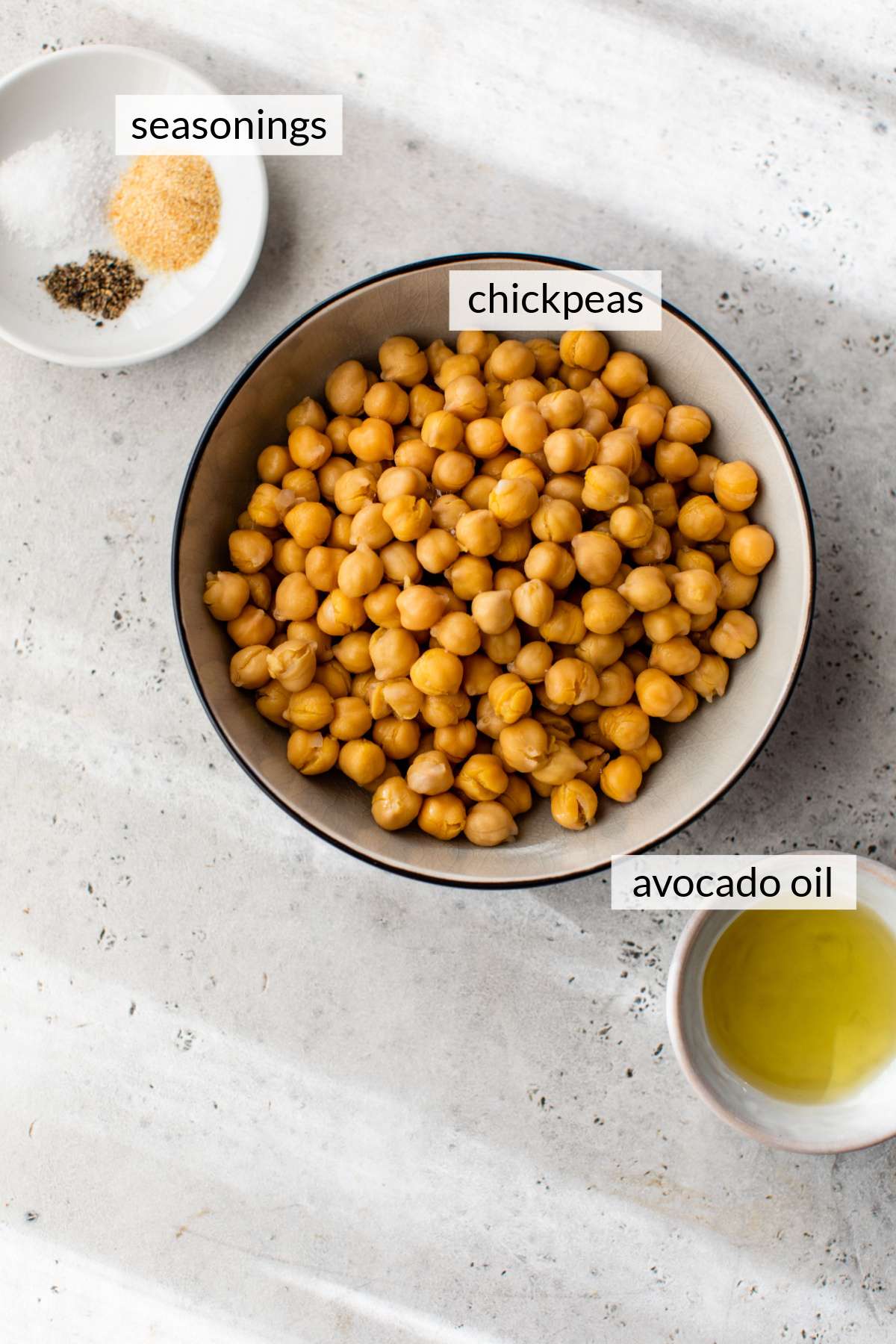 Chickpeas in a bowl near small bowls of seasonings and oil.