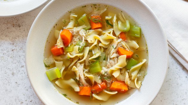 rotisserie chicken noodle soup in a white bowl and a gold spoon