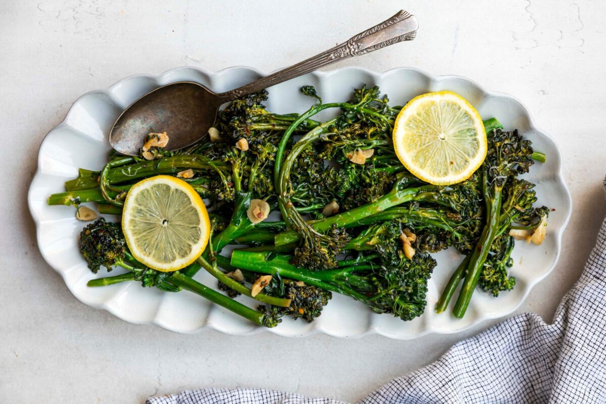 Sautéed broccolini on a white serving plate with slices of lemon.