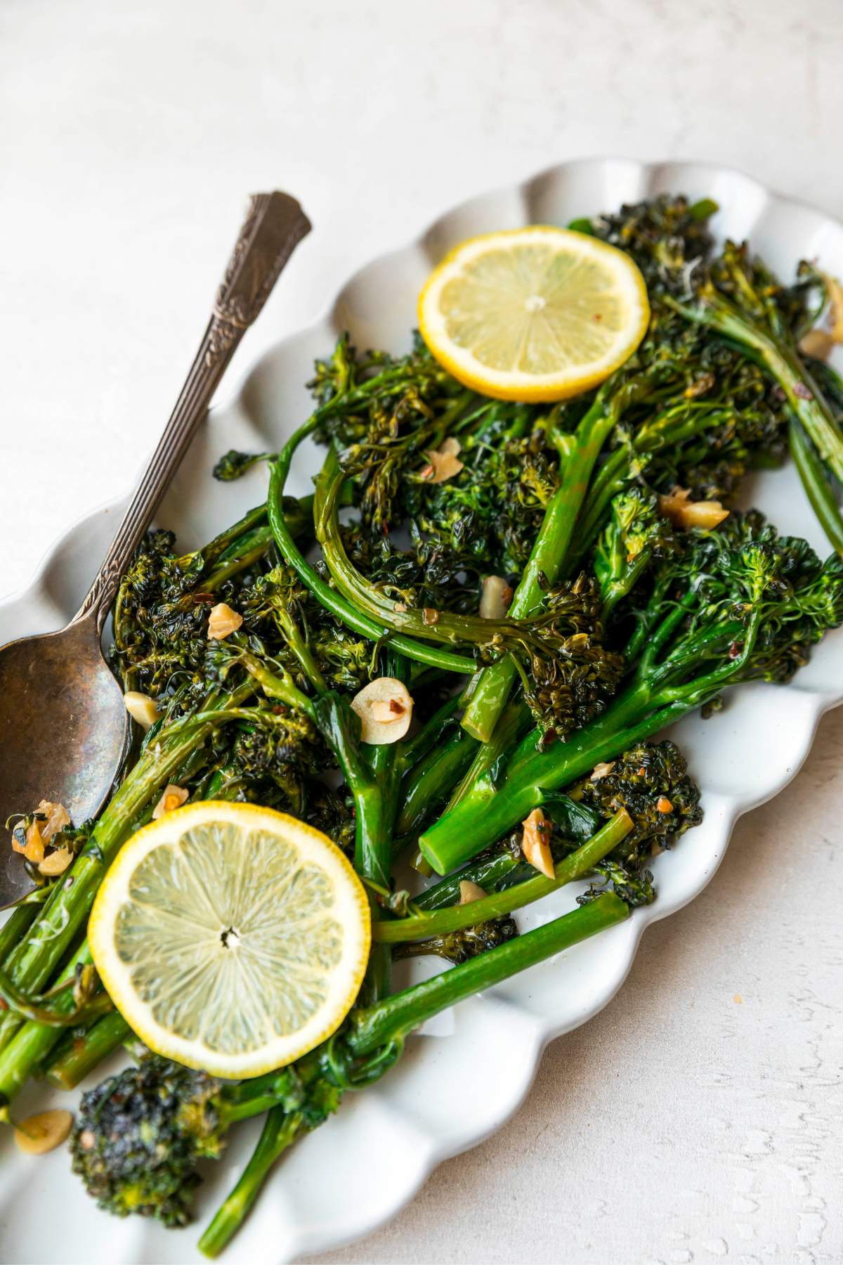 Sautéed broccolini on a white serving plate with slices of lemon.