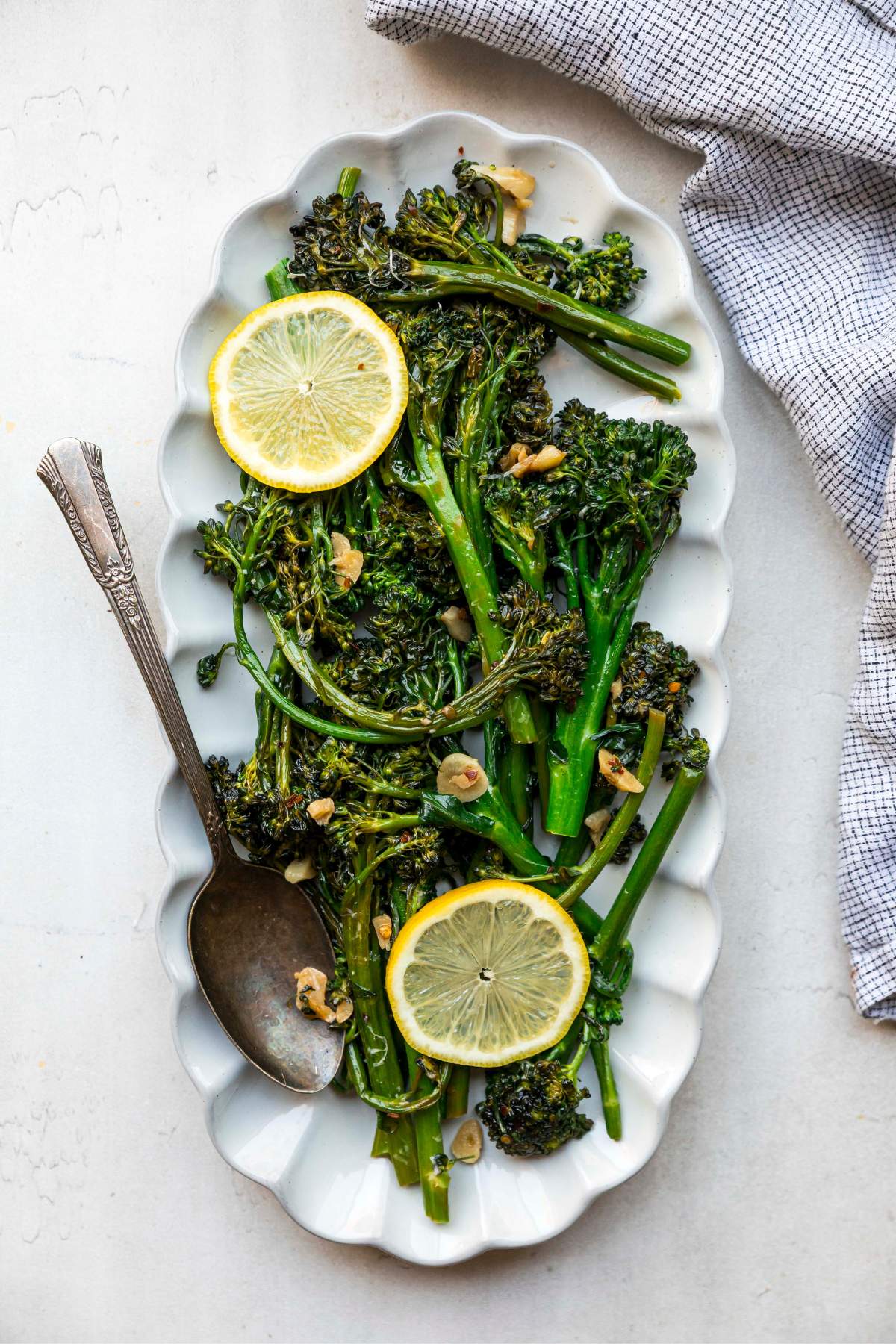 Sautéed broccolini served on a white plate with fresh lemon slices.