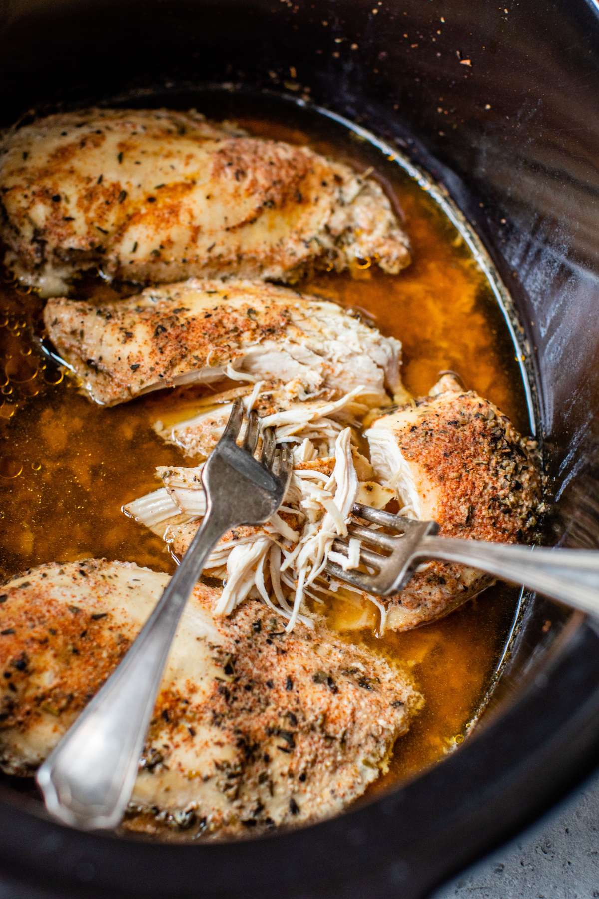 Two forks shredding chicken in a slow cooker.