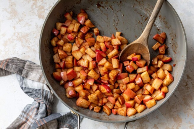 Stirring cinnamon apples with a wooden spoon in a skillet.