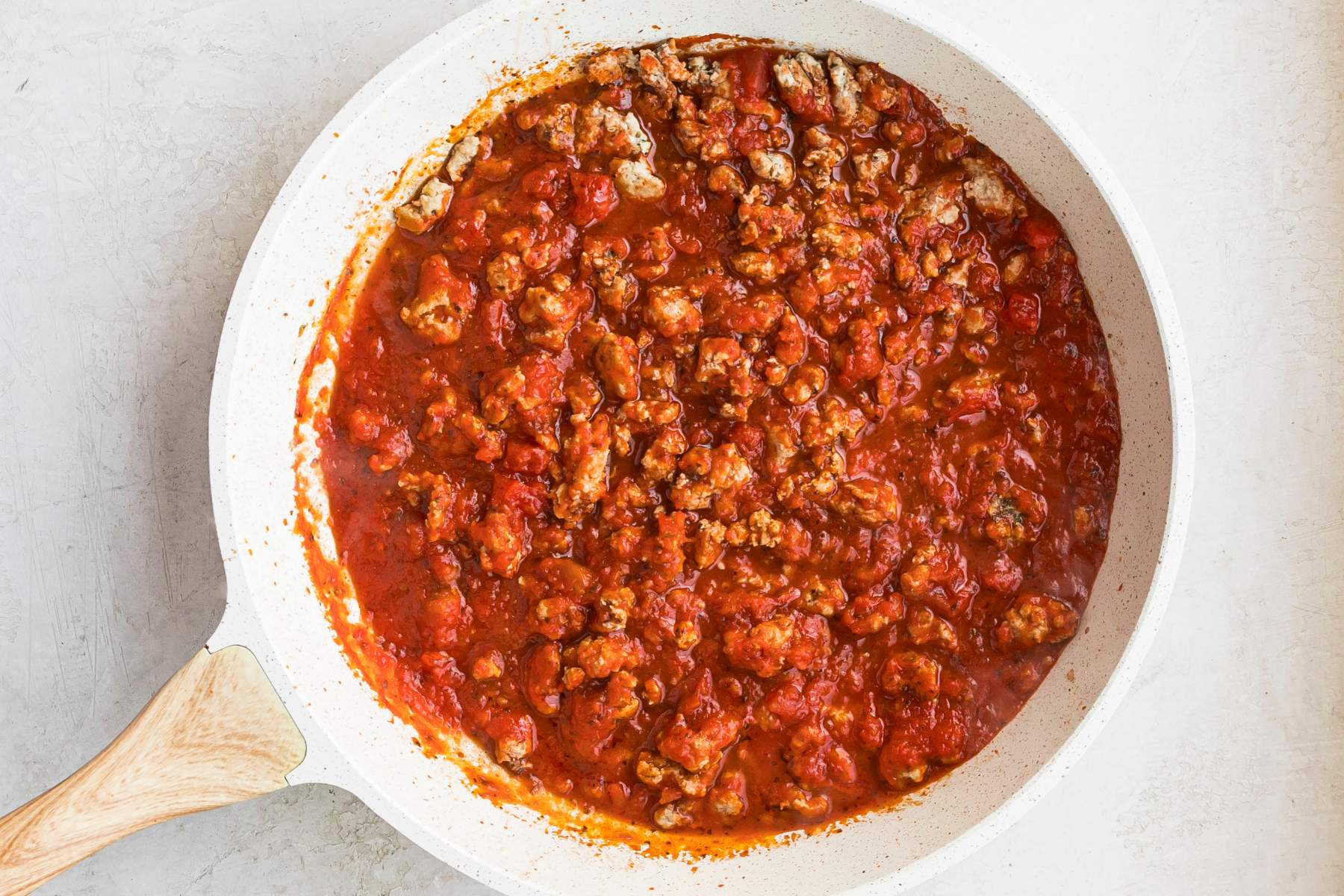 Tomato sauce cooking with ground turkey in a skillet.